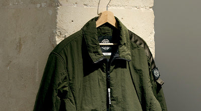 ST95 Lightweight Padded Overshirt in olive green, featuring zip closure, chest pocket, and sleeve logo badge.
