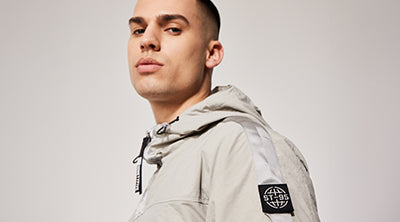 Model wearing the ST95 Dyne Smock in light grey, featuring sleeve logo patch, hood, and technical detailing.