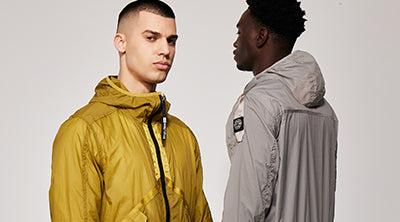 Two models wearing the ST95 Helio Hooded Blouson in yellow and grey, featuring lightweight fabric and logo detailing.