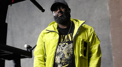 P Money wearing the ST95 Pulsar Anorak in bright yellow, styled with a graphic T-shirt and cap in an urban setting.