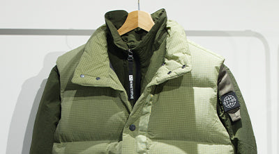 ST95 Puffer Vest in green displayed on a hanger, featuring quilted design, zip closure, and sleeve logo patch.