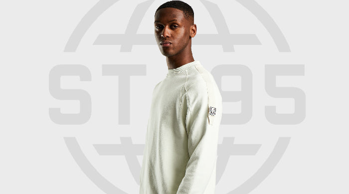 Model wearing the ST95 UV Reactive Sweat in off-white with sleeve logo patch, standing against a grey background with ST95 logo.