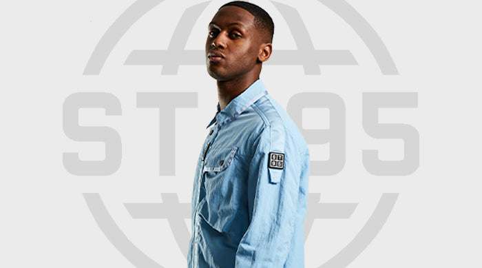 Model wearing the ST95 Ballute Overshirt in light blue with sleeve logo patch, standing against grey backdrop with ST95 logo.