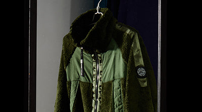 ST95 Zip Fleece in dark green hanging on a rail, featuring textured fabric, zip fastening, and sleeve logo patch.