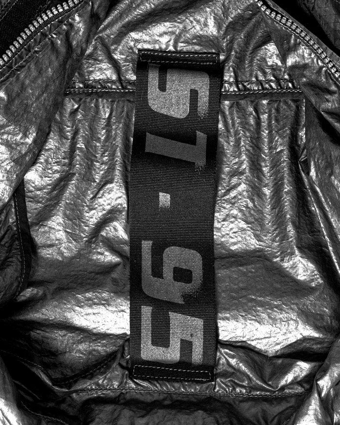 Close-up of black ST95 branded internal label stitched onto metallic technical fabric with visible texture and folds.