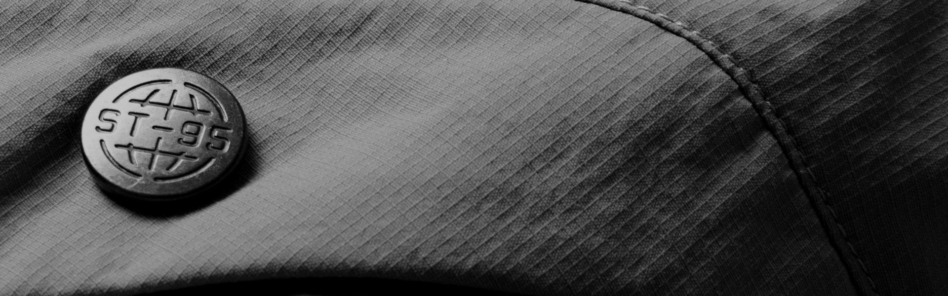 Close-up of ST95 branded metal button on technical ripstop fabric showing fine stitching and detailed texture.