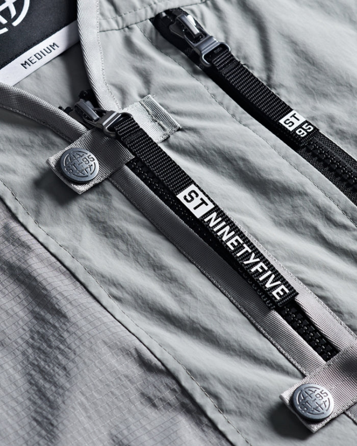 Close-up of ST95 design details showing branded zips, stitched logo buttons, and technical ripstop fabric texture.
