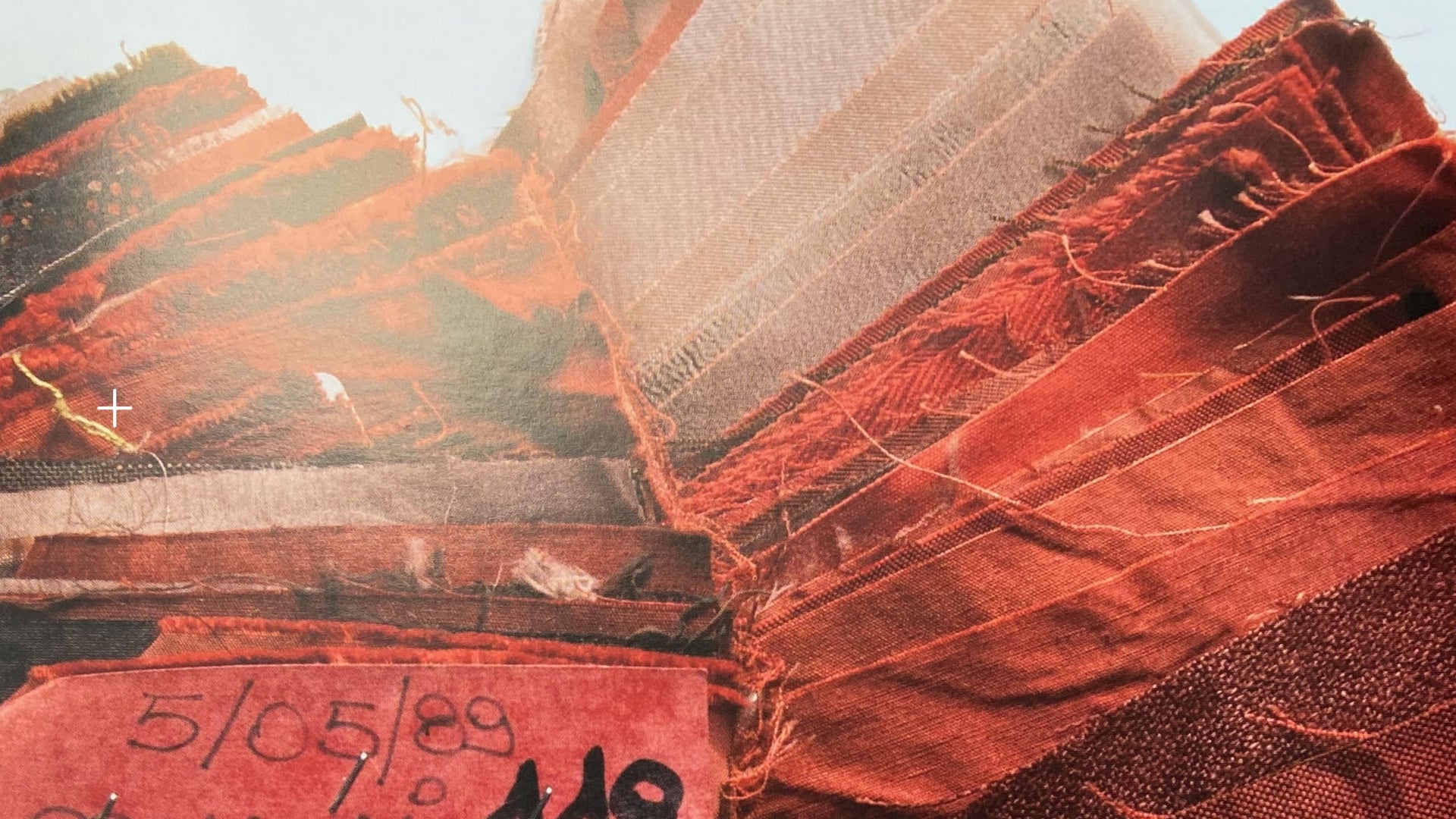 Close-up image of ST95 fabric swatches in red tones, showing textured weaves, frayed edges, and a dated sample tag.