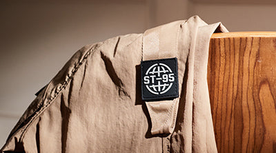 ST95 JP-8 Overshirt in light brown, featuring utility-style chest pockets, branded sleeve badge, and zip fastening.