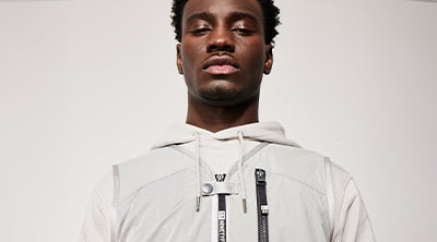 Model wearing the ST95 Delta Vest in light grey, featuring multiple front zips and technical detailing.