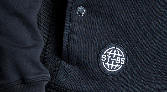 ChatGPT said:  Close-up of the ST95 logo patch on the sleeve of the Globe Pocket Hooded Sweat, showcasing garment detail and texture.