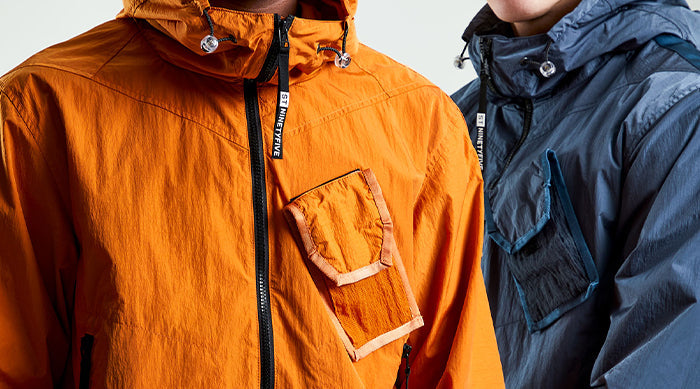 Models wearing the ST95 Horizon Anorak in orange and navy, featuring chest utility pocket and branded zip detailing.