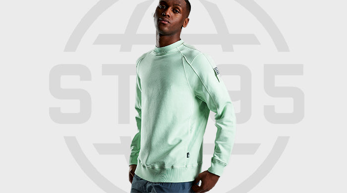 Model wearing the ST95 Crew Sweat in light green, featuring raglan sleeves, ribbed trims, and sleeve logo patch.