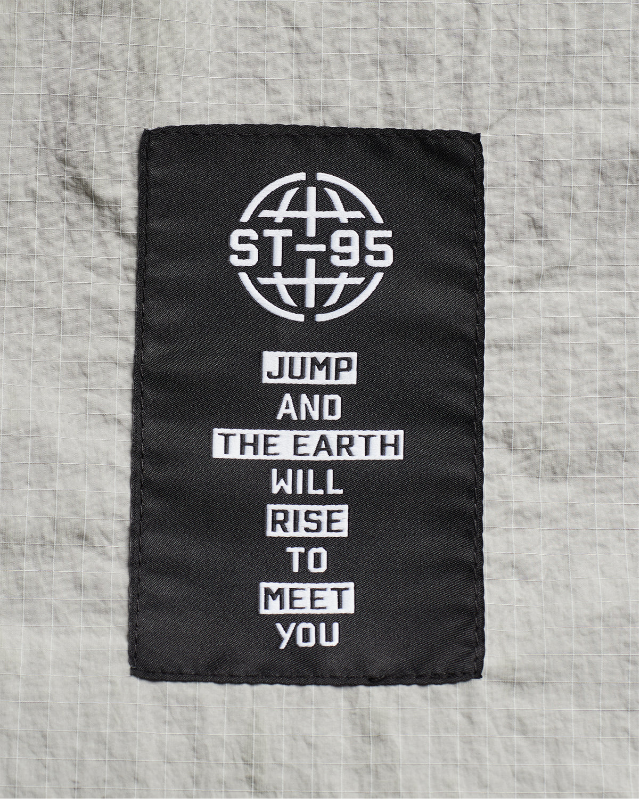 ST95 woven label in black with white text reading “Jump and the earth will rise to meet you” beneath globe logo.